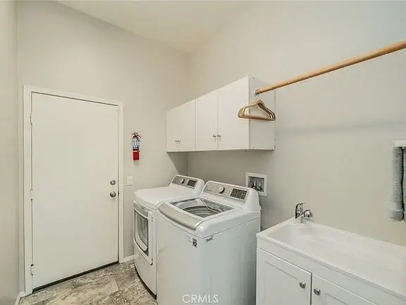 Laundry room with washer, dryer, utility sink, white cabinets, and exterior door
