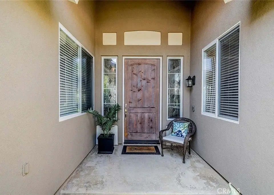 Front porch with wooden door, windows, potted plant, and chair