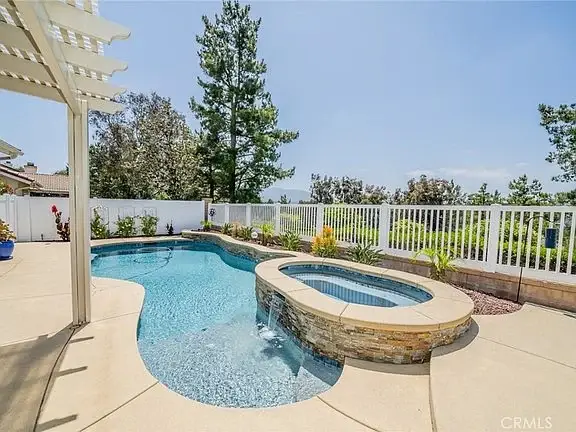 Swimming pool with spa, greenery, and white fence