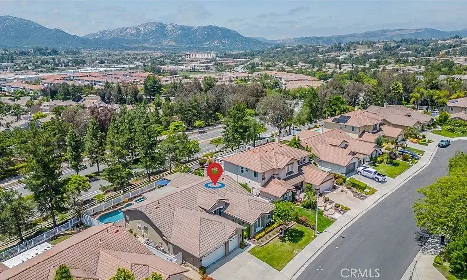 Aerial view of California real estate houses with brown rooftops, lawns, trees, hills, and cityscape, one marked by map pin