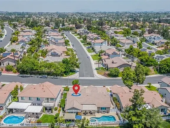 Aerial view of California real estate houses, streets, and greenery with one house marked by red pin