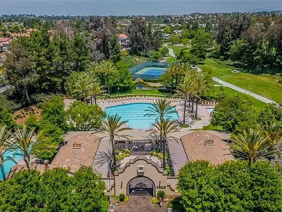 Aerial view of California real estate house with swimming pool, palm trees, tennis courts, and green landscaping