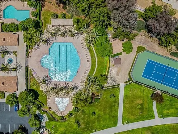 Aerial view of California real estate house with swimming pool, palm trees, tennis court, and landscaped green areas