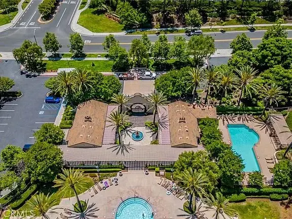Aerial view of California real estate house with pool, palm trees, and surrounding buildings