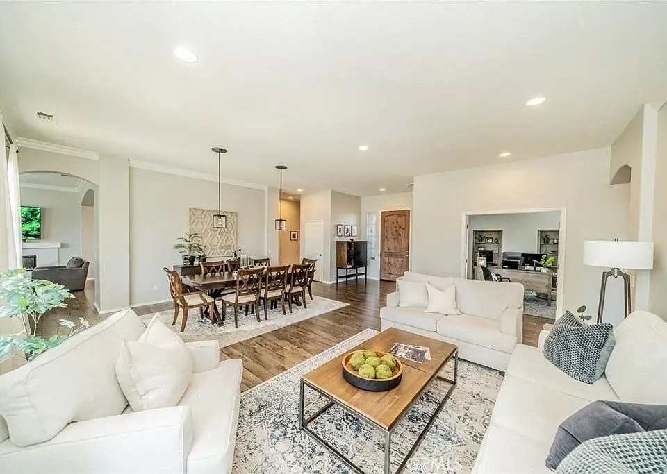 Living room with white sofa, wooden dining table, plants, and patterned rug