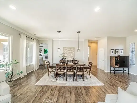 Dining room with large wooden table, chairs, windows, and wood flooring