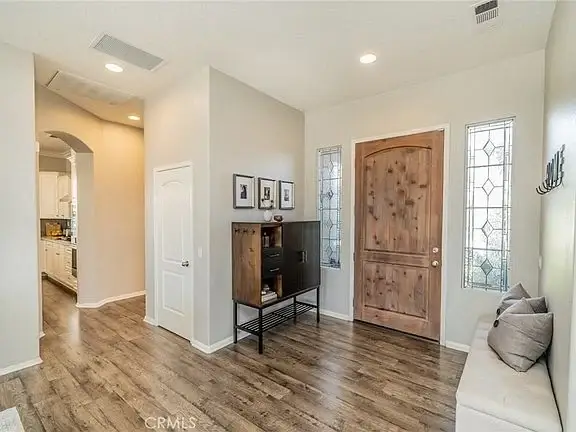 Entryway with wooden floor, front door, gray walls, console table, and bench