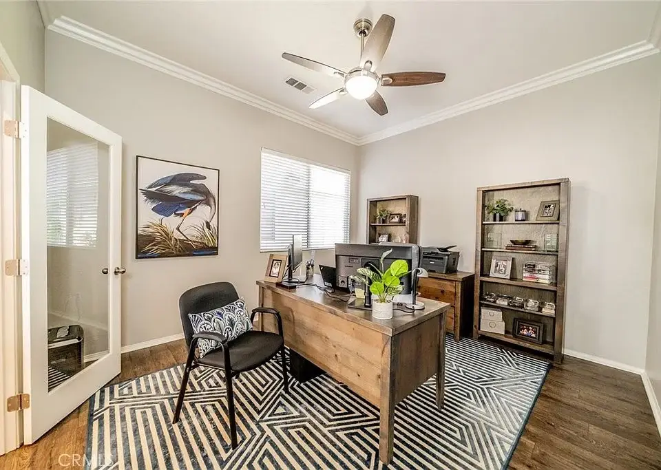 Office with wooden desk, black chair, shelves with decor, and patterned rug