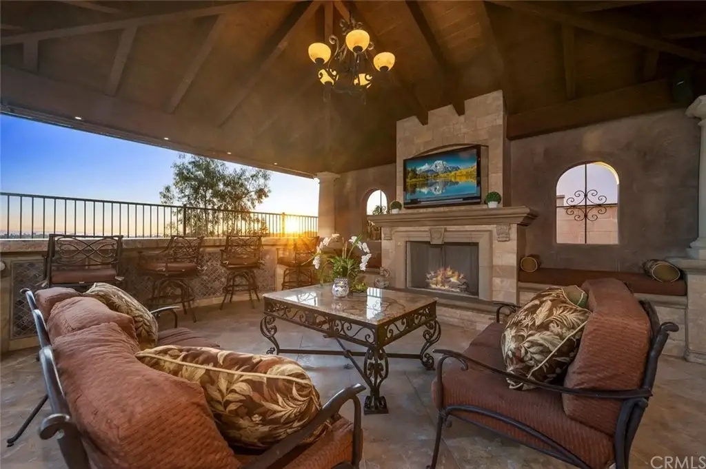 Patio of house California real estate with seating, fireplace, wall TV, chandelier, plants, and windows.
