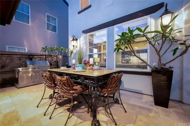 Outdoor dining area of house California real estate with table, chairs, grill, plants, and lights.