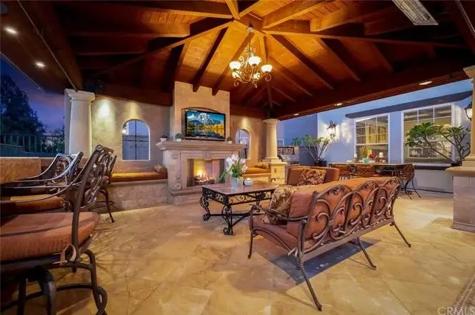 Patio of house California real estate with wood beam ceiling, seating, fireplace, and wall TV.