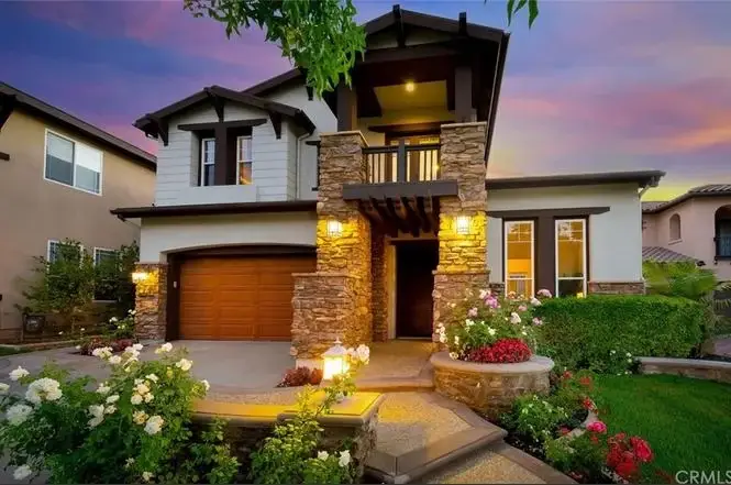 Two story house California real estate with stone facade, porch lights, and flower garden.