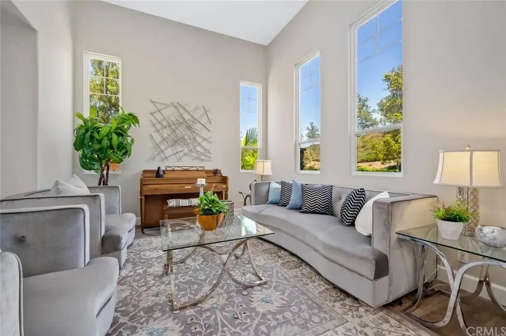 Living room with gray sectional sofa, armchairs, glass coffee table, piano, plant, and large windows.
