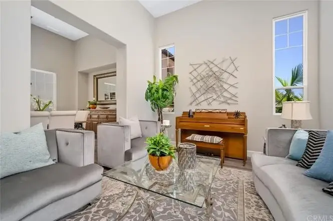 Living room with gray sofas, glass coffee table, patterned rug, piano, and large windows.