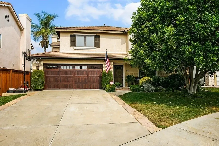 Two-story California real estate house with front yard, driveway, American flag, and surrounding trees