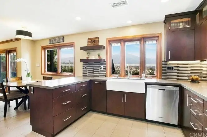 Kitchen with dark wood cabinets, large window, stainless steel refrigerator, farmhouse sink, and light countertop