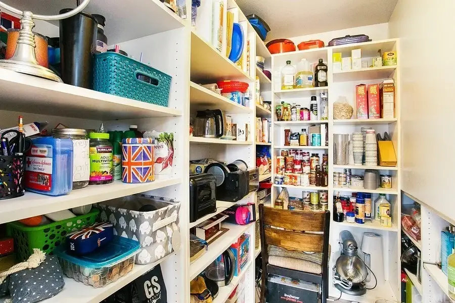 Pantry with shelves holding canned goods, jars, snacks, and kitchen appliances.