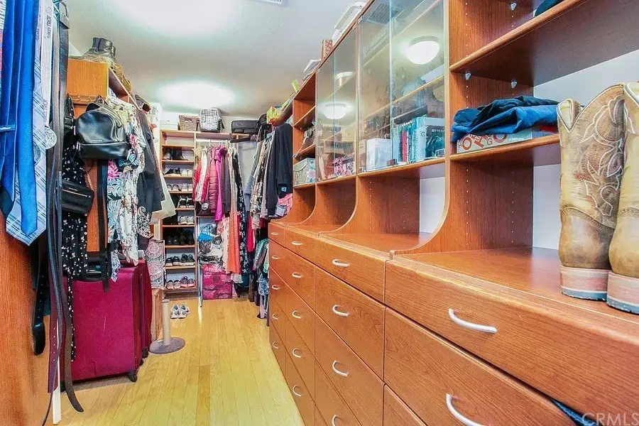 Walk-in closet with wooden drawers, shelves with clothing and accessories, and cowboy boots at the end.