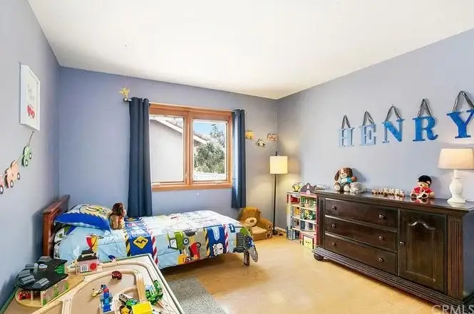 Kids bedroom with blue walls, bed with colorful bedding, dresser, toys, window, and name Henry on wall.
