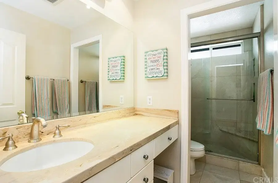 Bathroom with marble counter, sink, mirrors, glass shower, wall signs, and towels.
