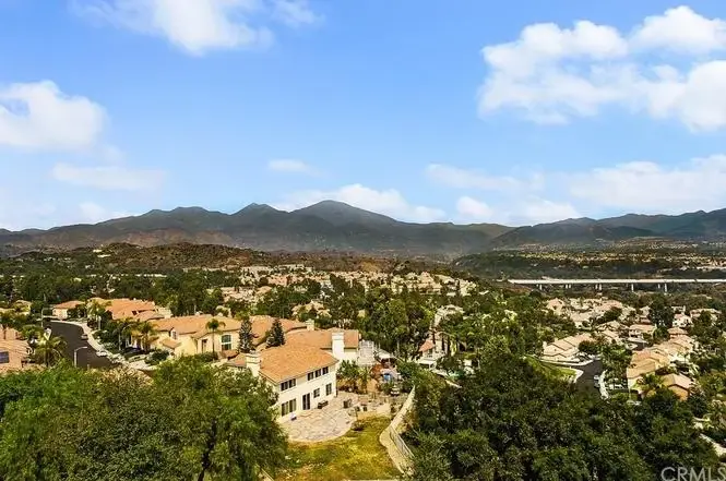 View of houses California real estate with trees, mountains, and cloudy sky.