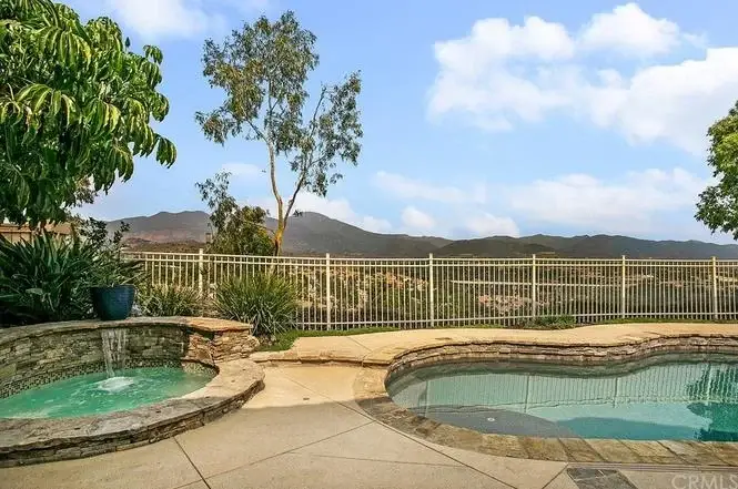 Pool area with stone hot tub, waterfall, greenery, and mountains in the background.