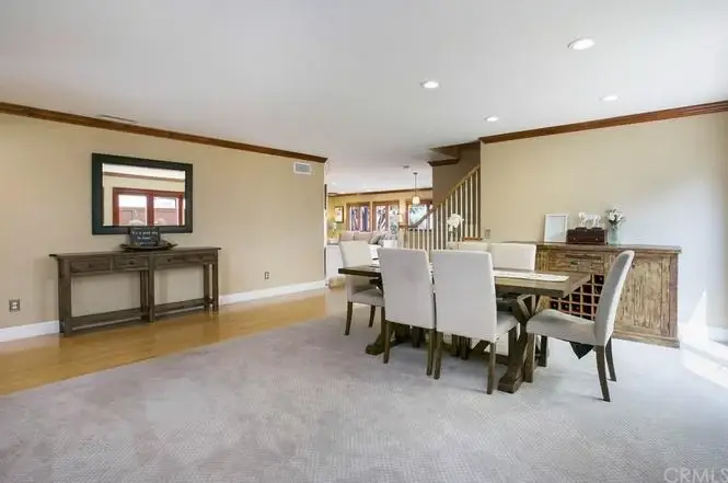dining area with wooden table and chairs, neutral walls, carpet, sideboard, staircase, and large windows.