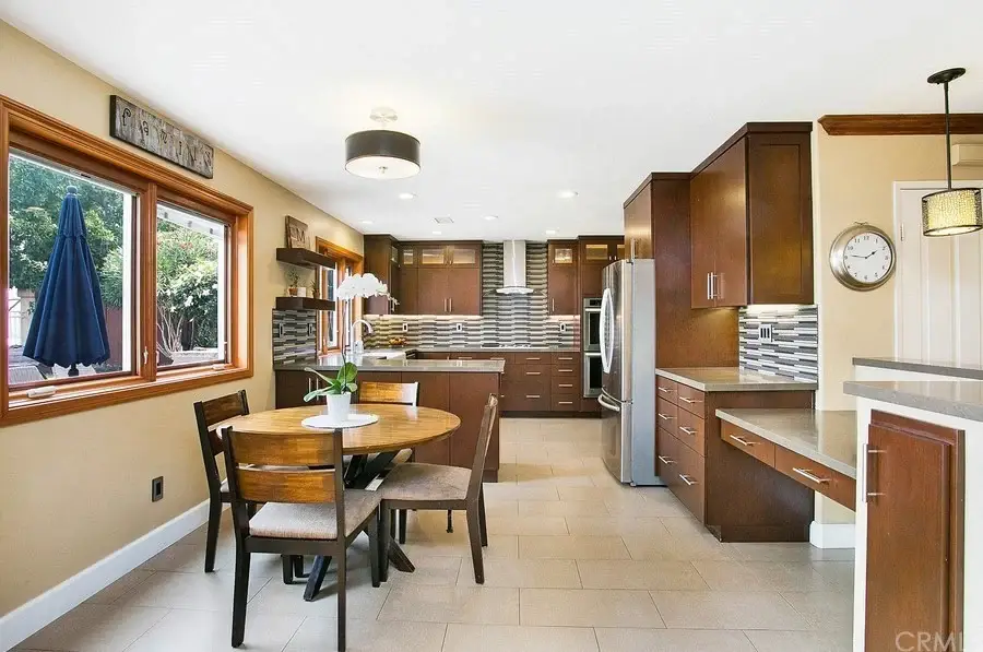 Kitchen with wooden cabinets, round dining table with four chairs, window with outdoor view, tile floor, and stainless steel appliances.