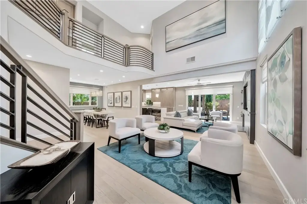 Living room with high ceiling, white chairs, round coffee table, rug, wall art, and large windows.