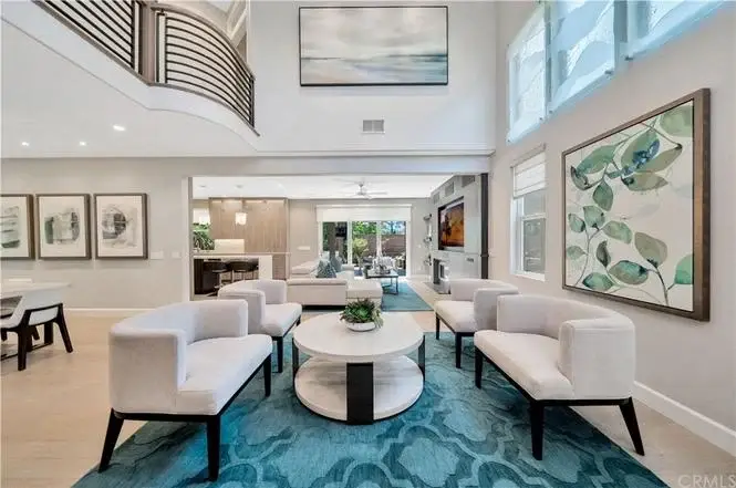 Living room with two white chairs, round coffee table, blue rug, wall art, and large windows.