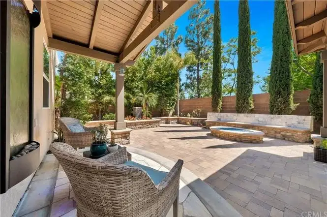 Patio of house California real estate with woven chairs, stone fire pit, and plants.
