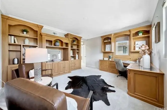Home office with wood shelves, desk and chair, leather armchair, cowhide rug, and carpet floor.