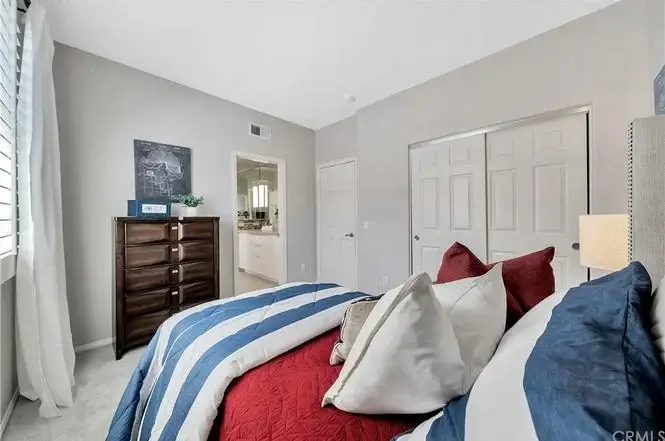 Bedroom with red and blue striped bed, pillows, chest of drawers, and doorway.