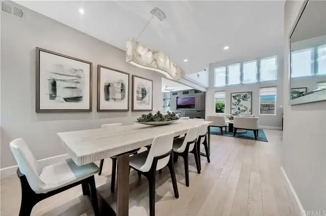 Dining area with light wood table, white chairs, abstract wall art, and large windows.
