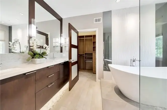 Bathroom with double vanity, dark wood cabinets, freestanding tub, glass shower, windows, and plants.
