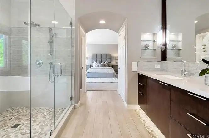 Bathroom with glass shower, freestanding tub, double vanity with dark wood cabinets, tile floor, and doorway to bedroom.