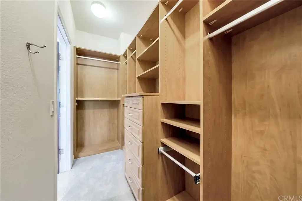Walk in closet with wood shelves, drawers, hanging rods, and light floor.