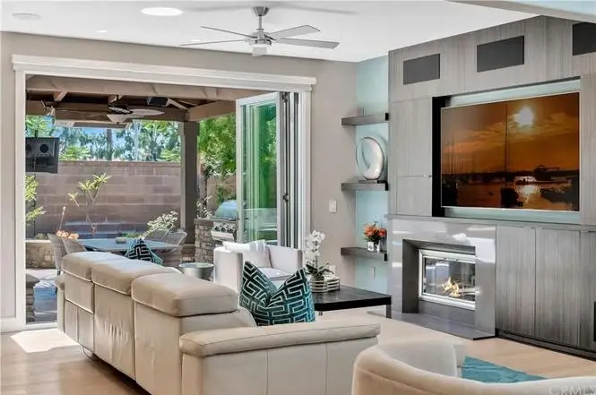 Living room with light sofa, pillows, wall TV, fireplace, and glass doors to pool patio.