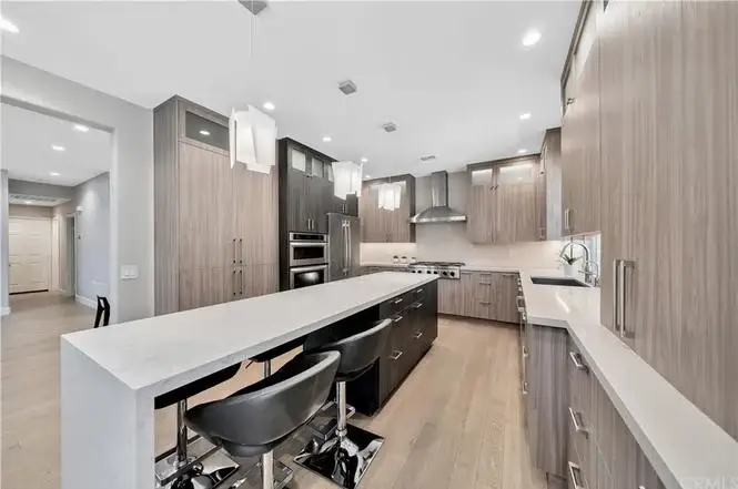 Kitchen with large island, wood and gray cabinets, stainless steel appliances, and pendant lights.