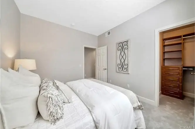 Bedroom with large bed, white duvet, pillows, bedside lamp, and open closet with wood shelves.
