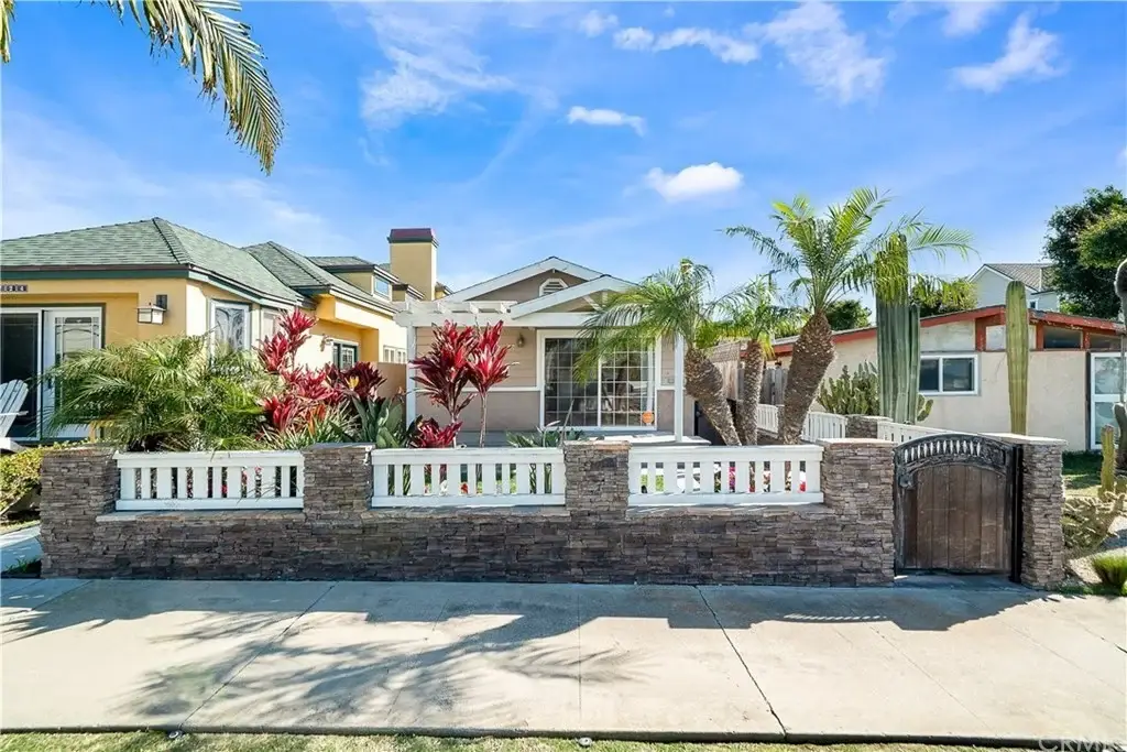 California real estate house with front yard, plants, palm trees, and stone wall