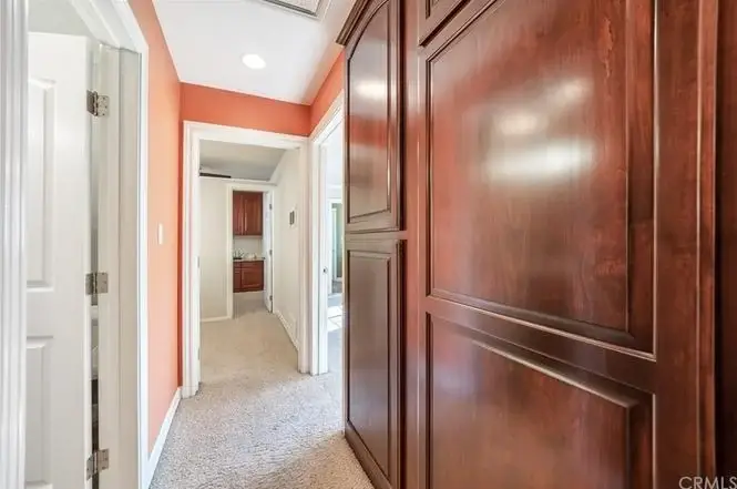 Hallway with carpet, wooden cabinet, orange walls, and doors to rooms on both sides