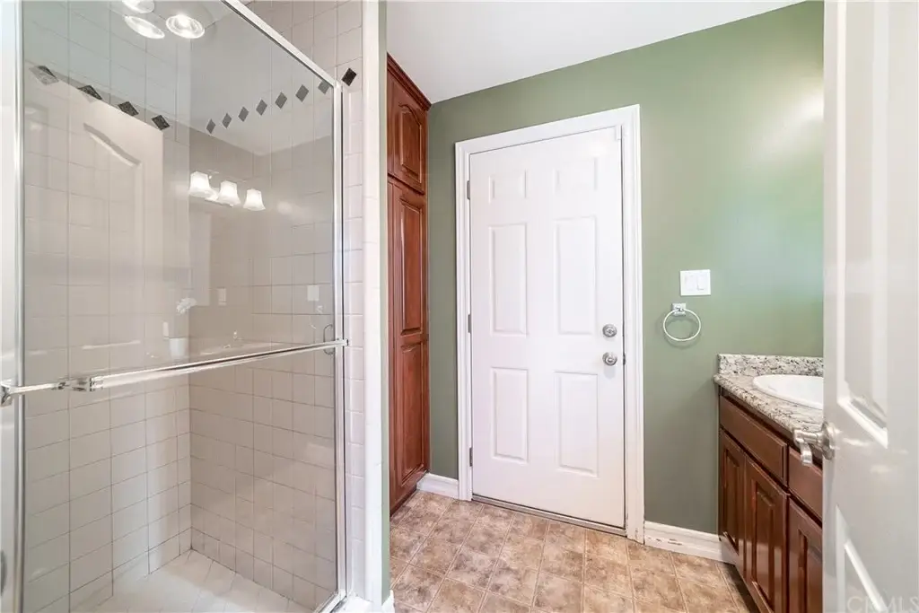 athroom with glass shower, green walls, wooden cabinets, tiled floor, and a door