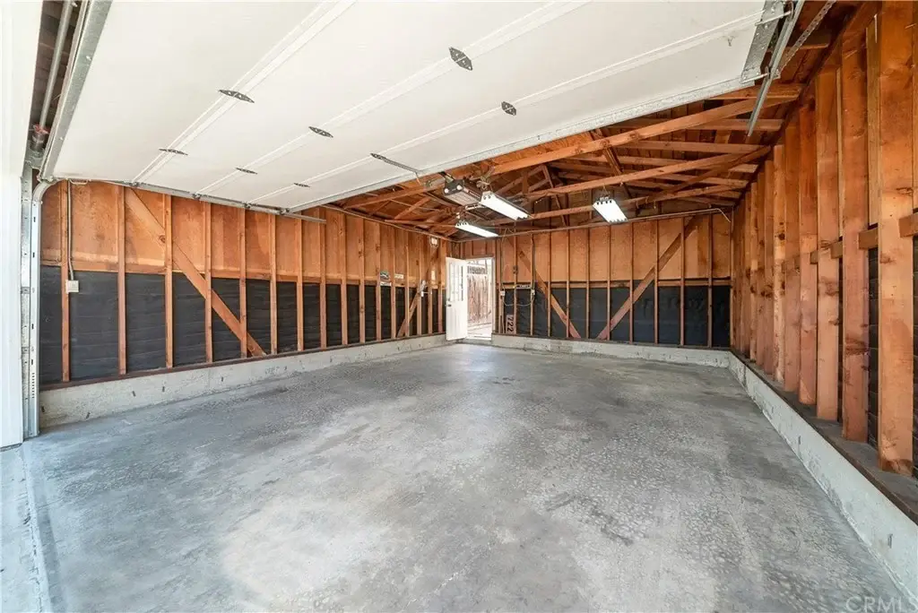 Garage with exposed wooden beams, concrete floor, unfinished walls, and door to outside