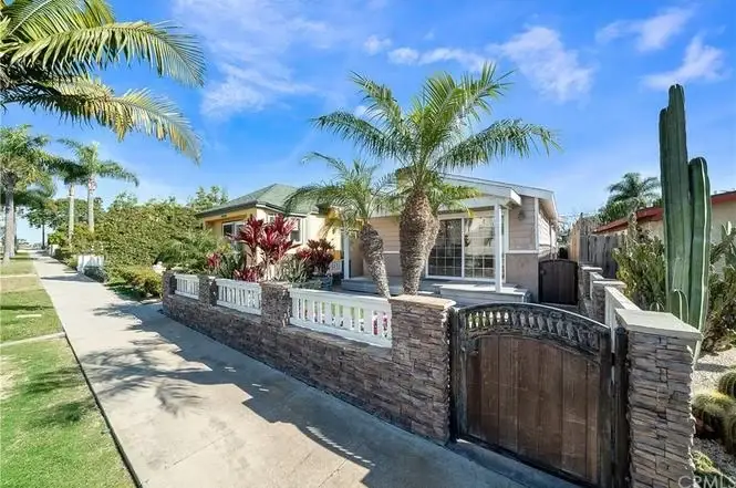 California real estate house with front yard, palm trees, landscaping, stone wall, and gate