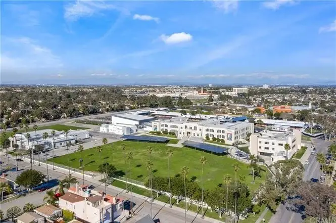 Aerial view of open area with buildings, green fields, palm trees, and California city around it.