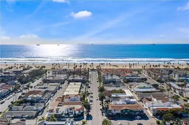 Aerial view of large white building complex with green grass, palm trees, and California city buildings in the background.