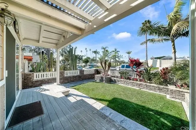 Backyard with wooden deck, landscaped garden, palm trees, and shrubs