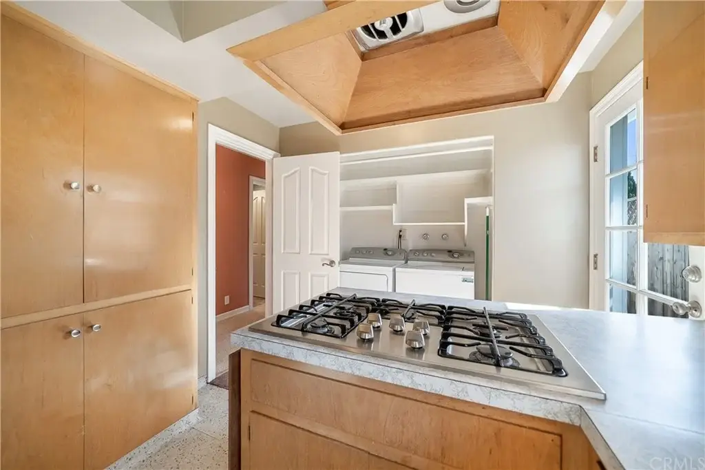 Kitchen with light wooden cabinets, gas stove, and view into laundry area