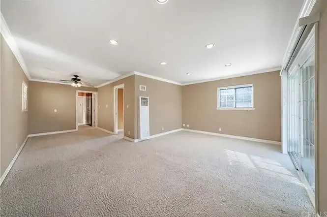Living room with beige walls, carpet, ceiling fan, window with blinds, and sliding glass doors to outdoor space